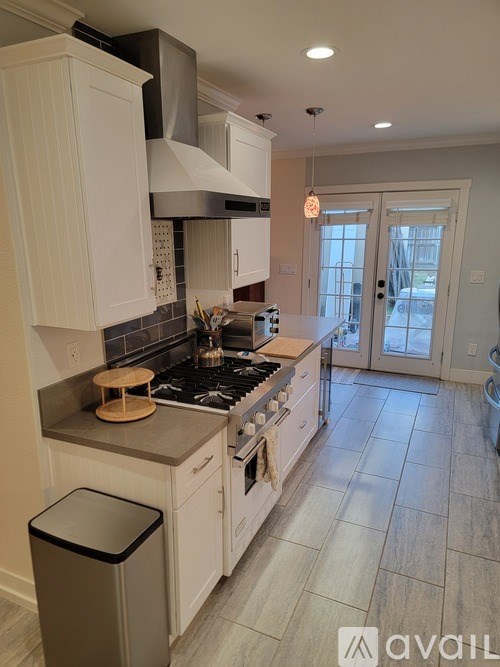 A kitchen with white cabinets and a black trash can.