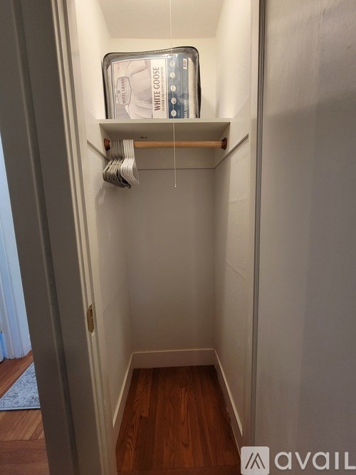 A white closet with a shelf and clothes hanging on a rod.