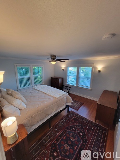 A bedroom with a bed, a rug, a ceiling fan, and a window with blinds.