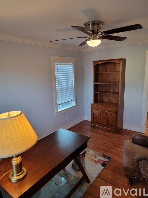 A room with a ceiling fan, a table with a lamp, and a chair.