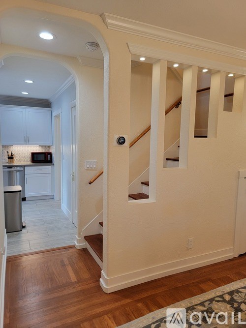 A hallway with a staircase and a kitchen in the background.