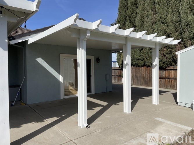 A patio area with a white pergola and concrete floor.