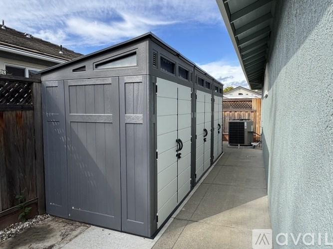 A grey storage shed with a door and windows is situated on a concrete pad.