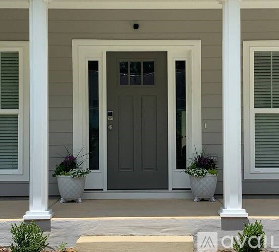 A grey front door is flanked by two potted plants.
