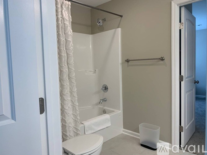 A white bathroom with a toilet, shower, and a white towel hanging on the shower rod.