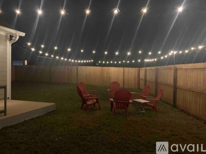 A backyard with a table and chairs under a string of lights.