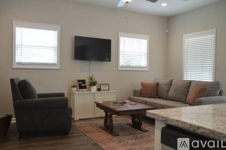 A living room with a grey couch, a black chair, a white cabinet, and a flat screen TV mounted on the wall.