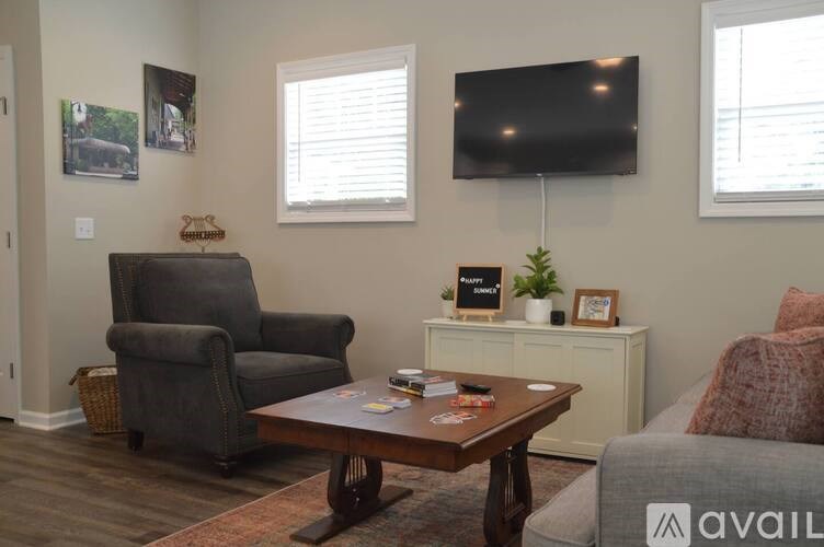 A living room with a grey couch, a brown coffee table, a grey armchair, a white TV stand with a plant on it, and pictures on the wall.