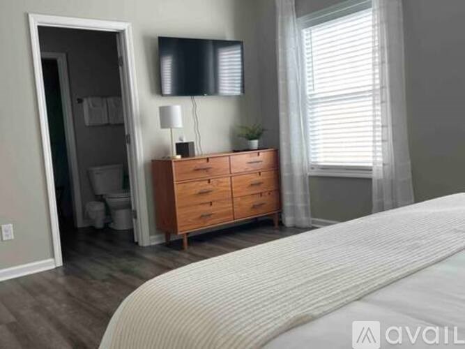 A bedroom with a large bed, a wooden dresser, and a bathroom visible through the door.