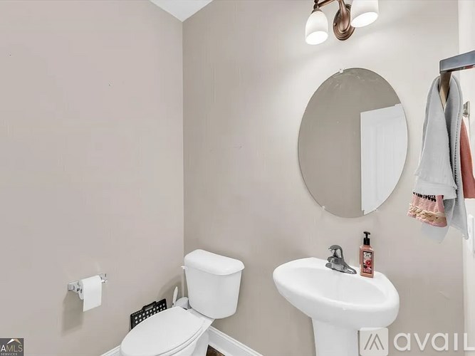 A bathroom with a toilet, sink, mirror, and a coat hanging on the wall.
