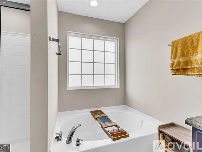 A white bathtub with a wooden tray on it and a window above.