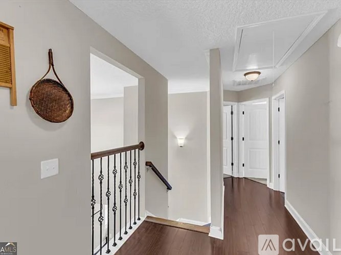 A hallway with a wooden floor, white walls, and a black railing.
