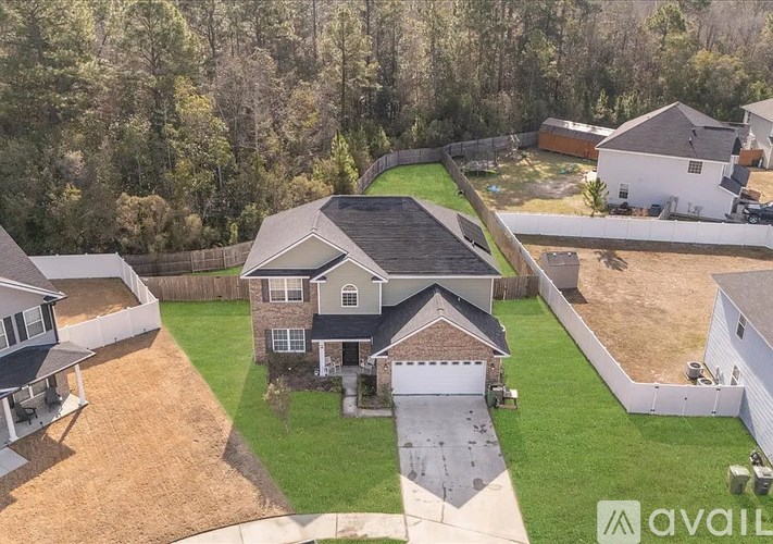 A house with a brown roof and a white garage door is surrounded by a fence and a green lawn.