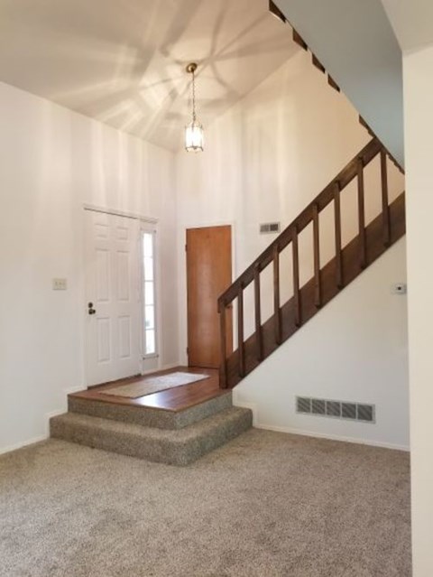A staircase with a wooden handrail leads up to a white door.