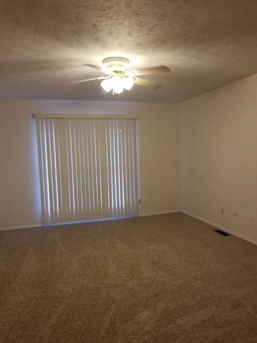 A room with a carpeted floor and a ceiling fan.