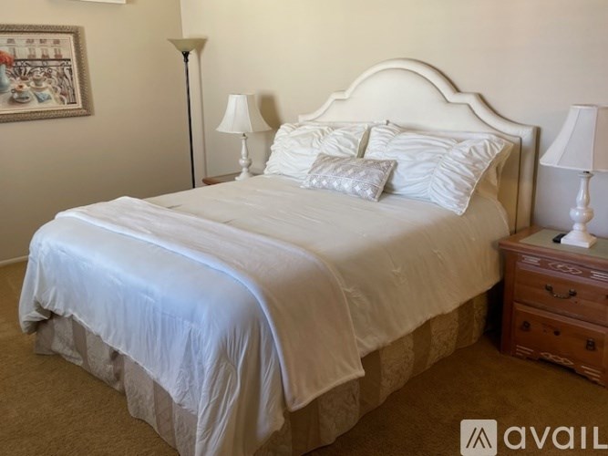 A bed with a white headboard and two pillows sits in a room with two lamps on either side.