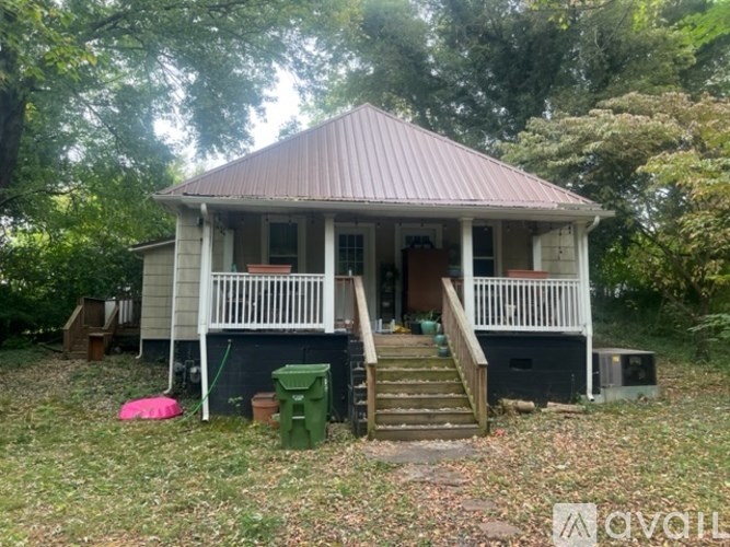 A small house with a porch and a green trash can sits in a grassy area.