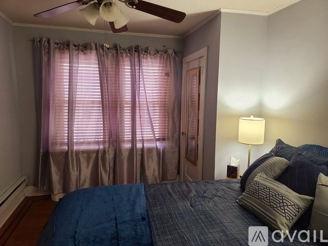 A bedroom with a bed, a ceiling fan, and a window with curtains.