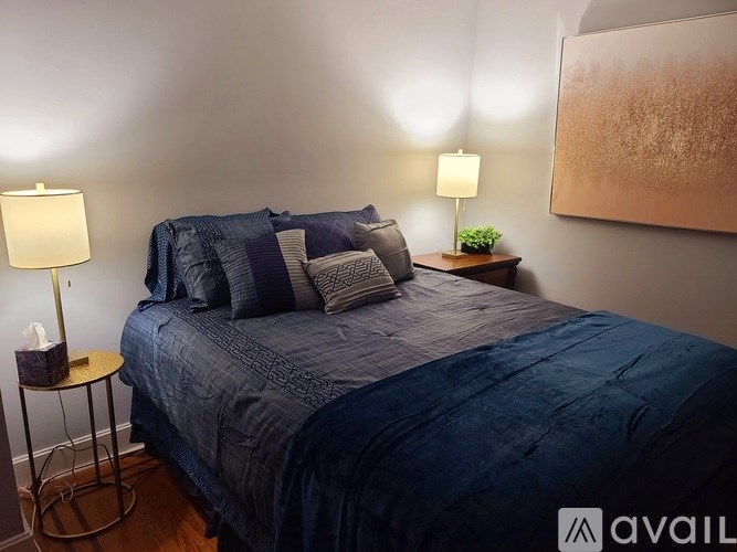 A bed with a blue comforter and pillows is in the foreground with two lamps on side tables.