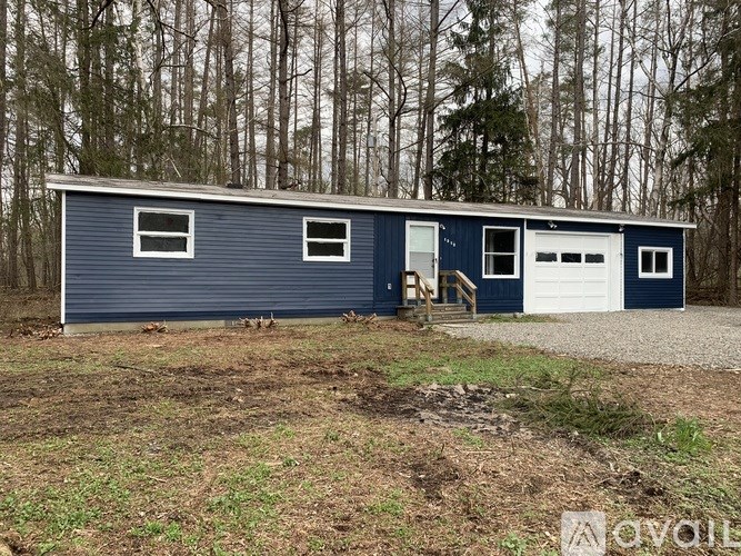 A blue two-car garage with a white door is situated in a wooded area.
