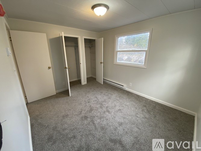 A carpeted room with a window and a door leading to another room.