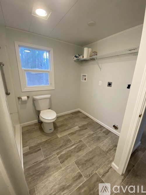 A bathroom with a toilet, a window, and a shelf with toilet paper.