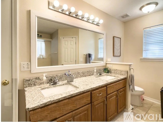 A bathroom with a marble countertop and a large mirror with lights above it.