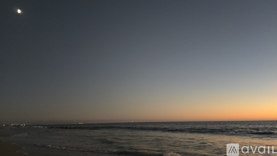 A beach scene at dusk with the moon visible in the sky.