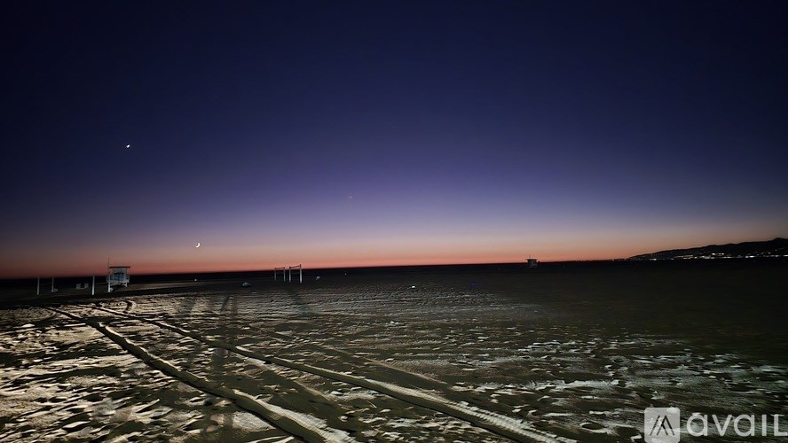 A dark sky with a few stars and a moon visible above a field with tire tracks.