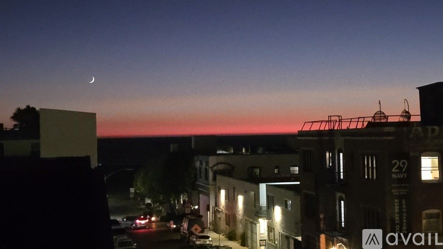 A cityscape at dusk with a crescent moon visible in the sky.
