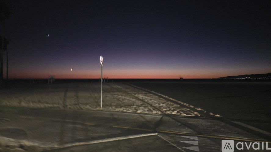 A pole stands in the middle of a parking lot at dusk.