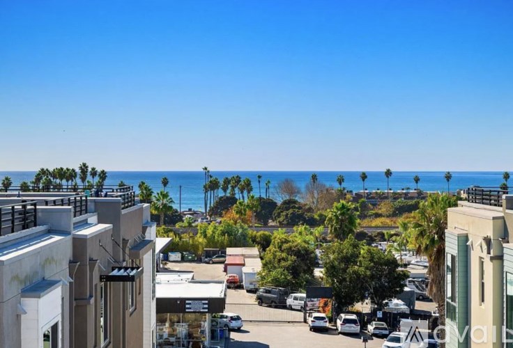 A view of a street with cars and buildings with a body of water in the background.