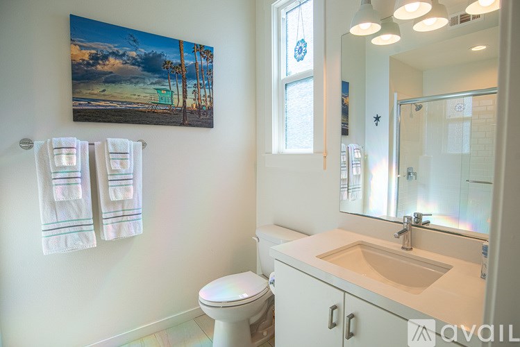 A bathroom with a toilet, sink, and a picture of a beach on the wall.