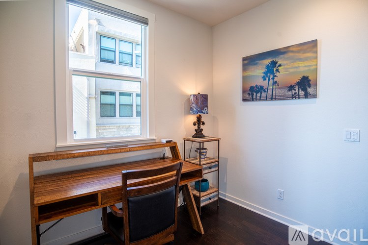 A room with a wooden desk and chair, a window, and a painting on the wall.