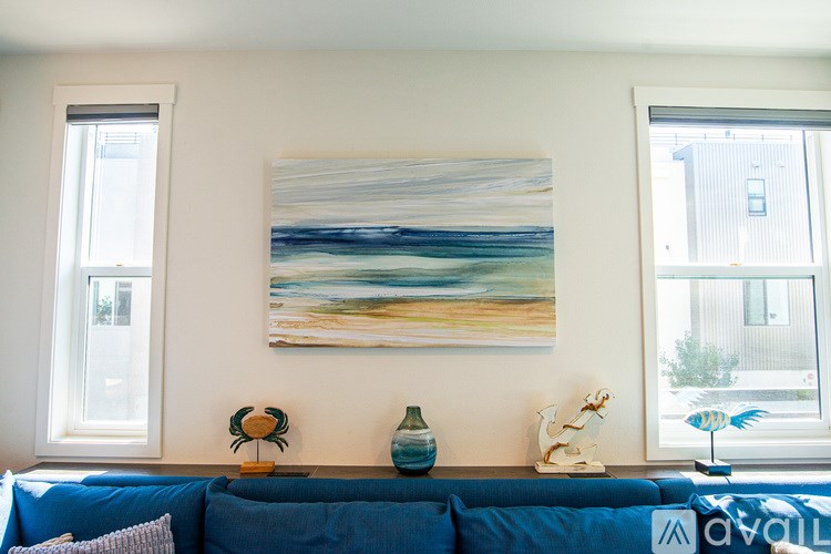 A blue couch with a painting on the wall above it.