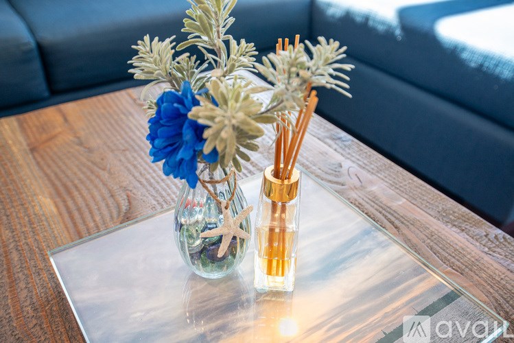 A vase with blue flowers and branches sits on a glass table.