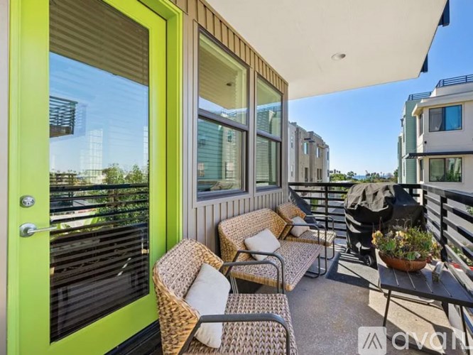 A balcony with a green door, wicker chairs, and a table with a potted plant.
