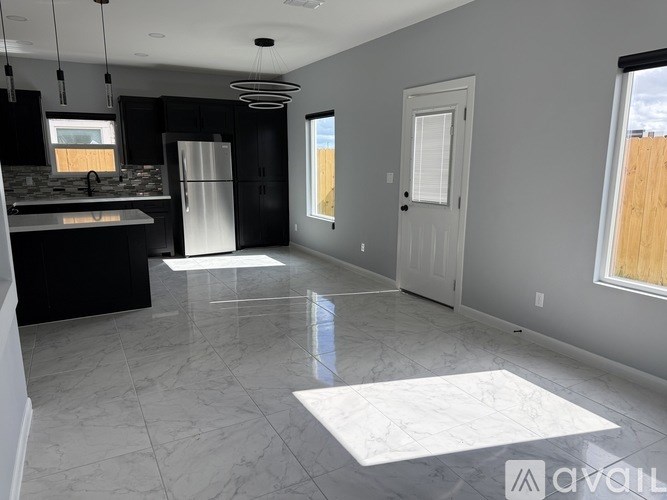 A spacious kitchen and living room with a marble floor and a view of the outdoors through the windows.