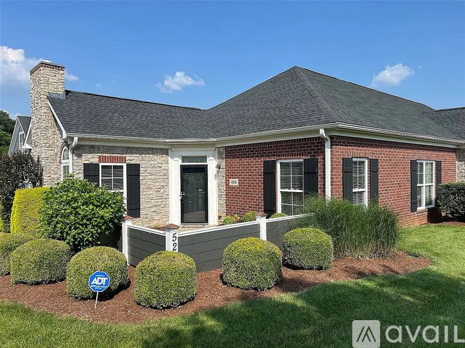 A house with a brick facade and a black door is surrounded by bushes and has a sign that says "ADT" in the front yard.