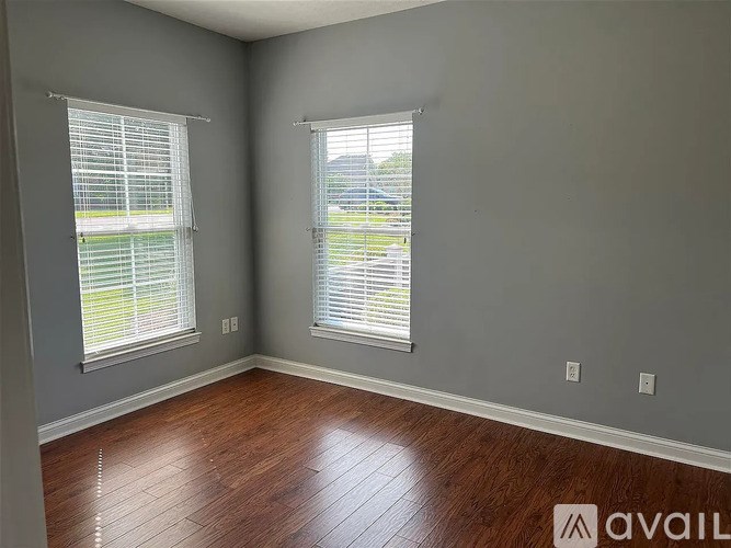 A room with wooden floors and two windows with blinds.