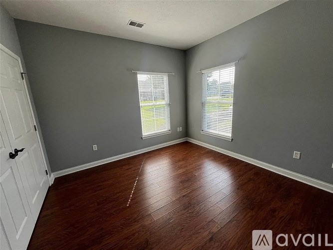 A room with wooden flooring and two windows.