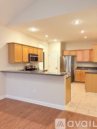 A spacious room with wooden flooring and a kitchen area in the background.