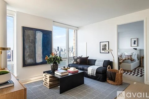 A living room with a black couch and a large painting on the wall.