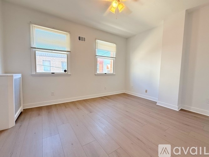 A room with wooden flooring and two windows.