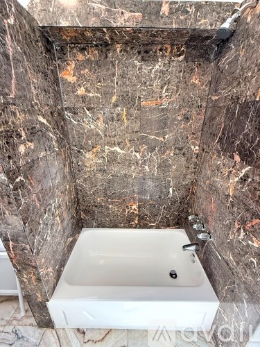 A white bathroom sink sits under a marbled wall.
