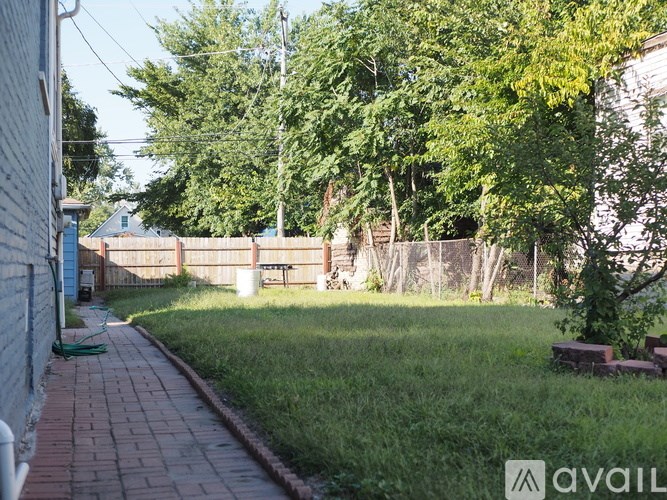 A backyard with a brick walkway, green grass, and trees.