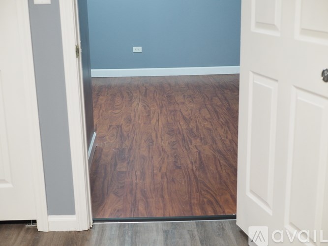 A white door is open to a room with wood flooring.