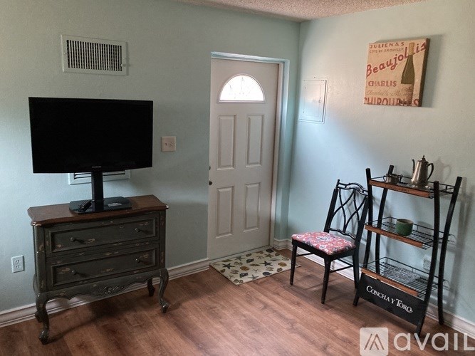 A room with a TV on a dresser and a chair with a floral cushion.