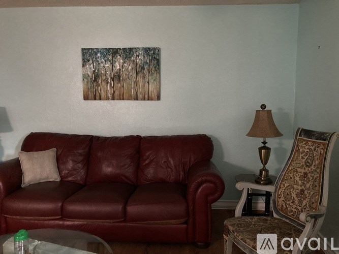 A red leather couch sits in a living room with a painting on the wall and a chair with a patterned upholstery.
