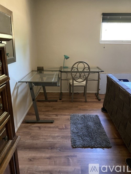A glass table with a metal base and a metal chair in a room with wooden flooring.